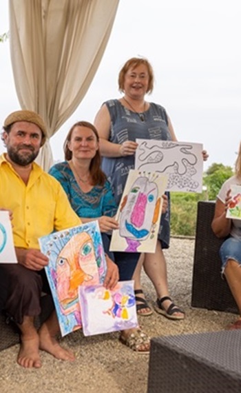 Henry Goldborn mit Teilnehmerinnen sitzend und Bilder hoch haltend, Workshop inneres Wachstum