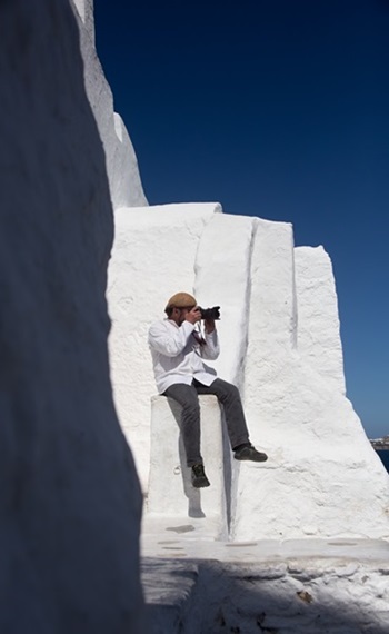 Henry Goldborn auf weißem Mauervorsprung sitzend beim Fotografieren, Mykonos